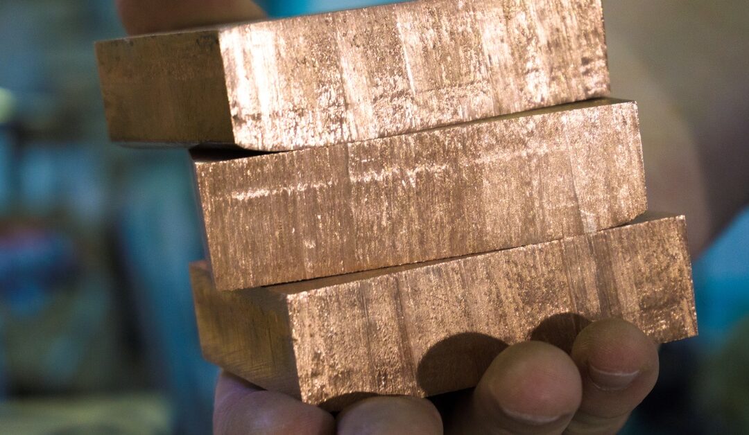 A person holds three blocks of copper in their hand. The material shines in the light, revealing its composition.